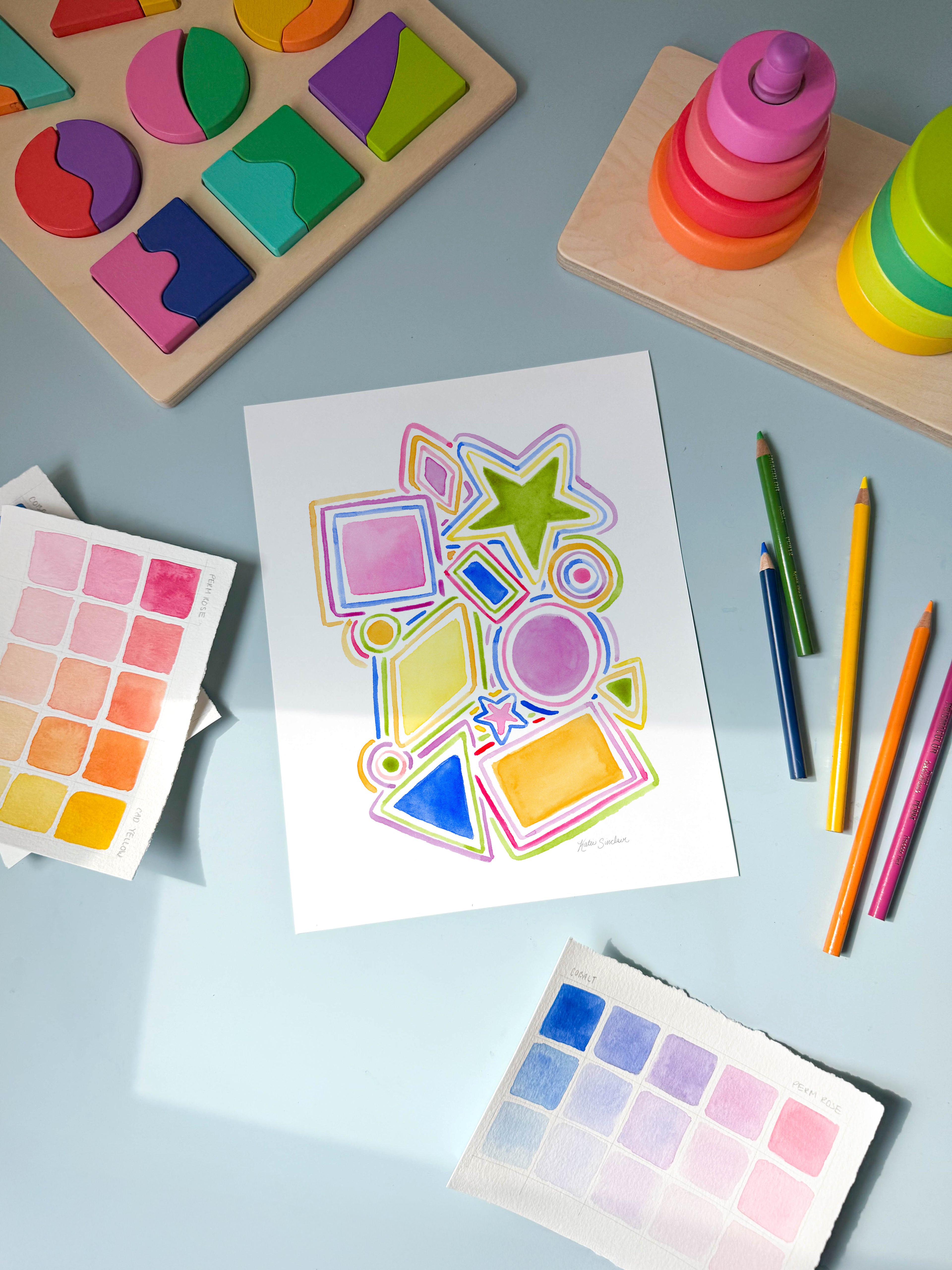 shapes and lines watercolor archival print by Katie Sinclair on a desk with colored pencils and a wooden puzzle.