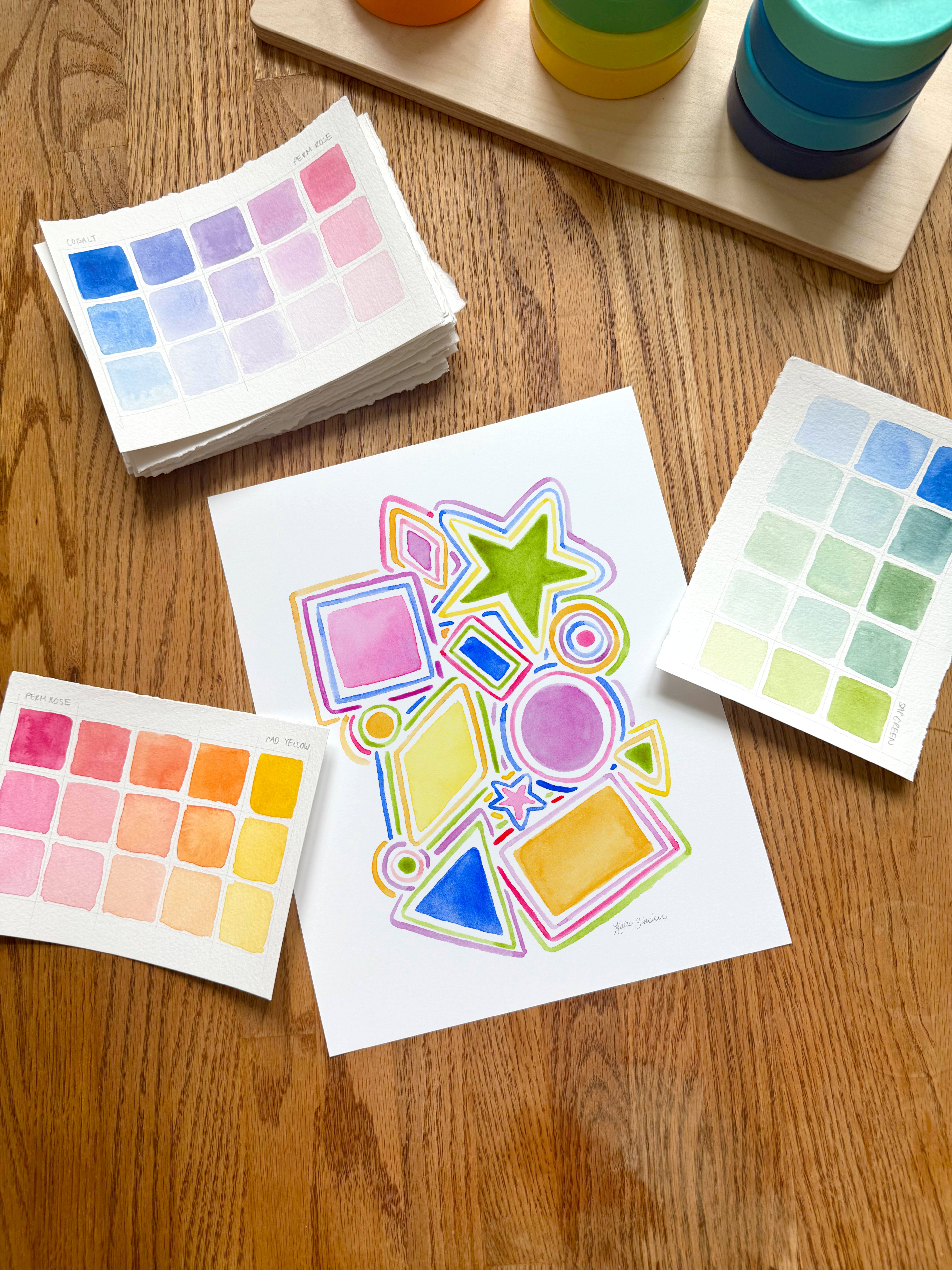 colorful watercolor shapes and lines archival print, surrounded by geometric toys on a wooden surface.  hand-painted by katie sinclair and perfect for a playroom or kid bedroom.
