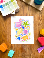 colorful watercolor shapes and lines archival print, surrounded by geometric toys on a wooden surface.  hand-painted by katie sinclair and perfect for a playroom or kid bedroom.
