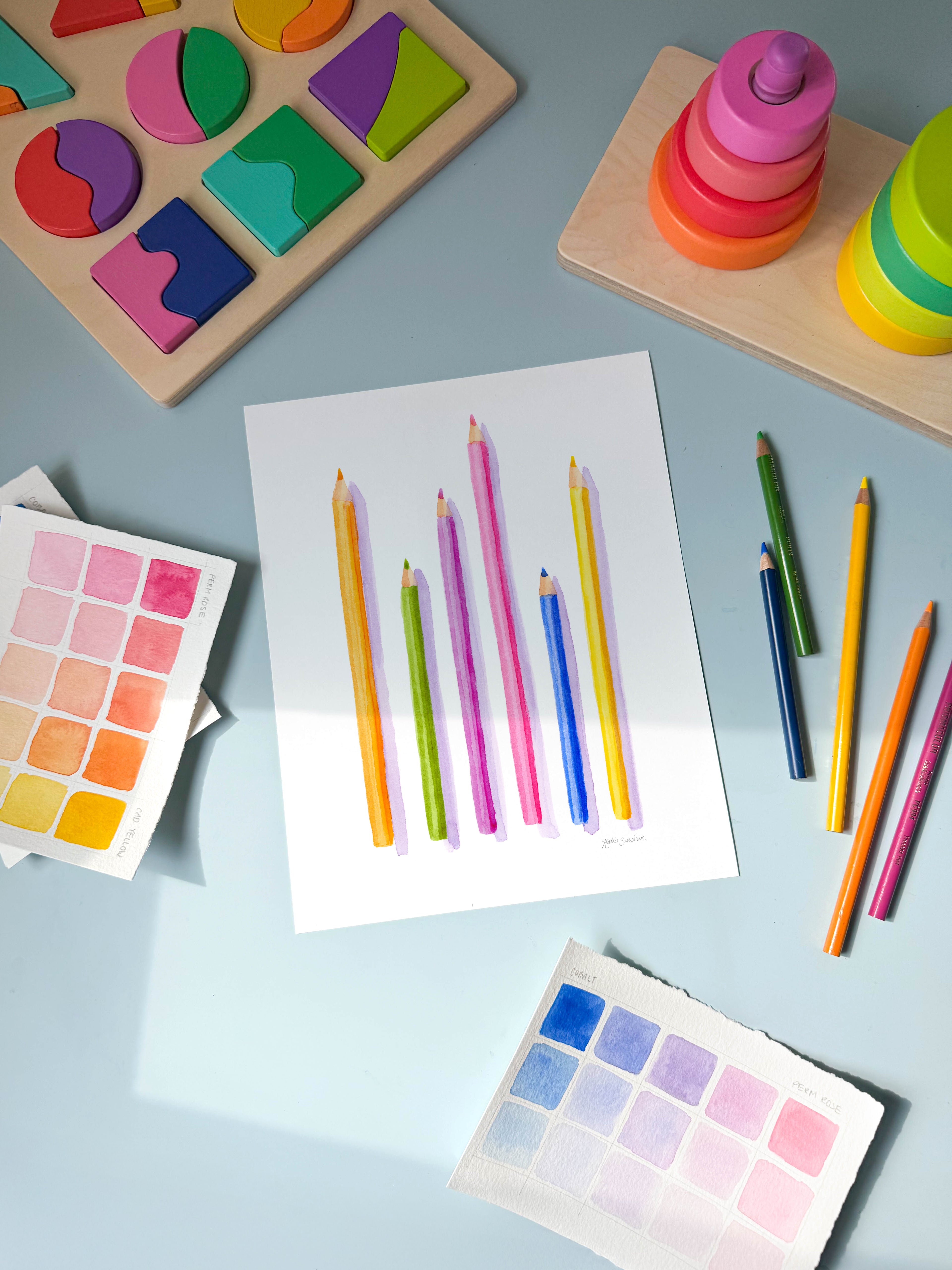 colored pencils watercolor archival print by Katie Sinclair on a desk with colored pencils and a wooden puzzle.