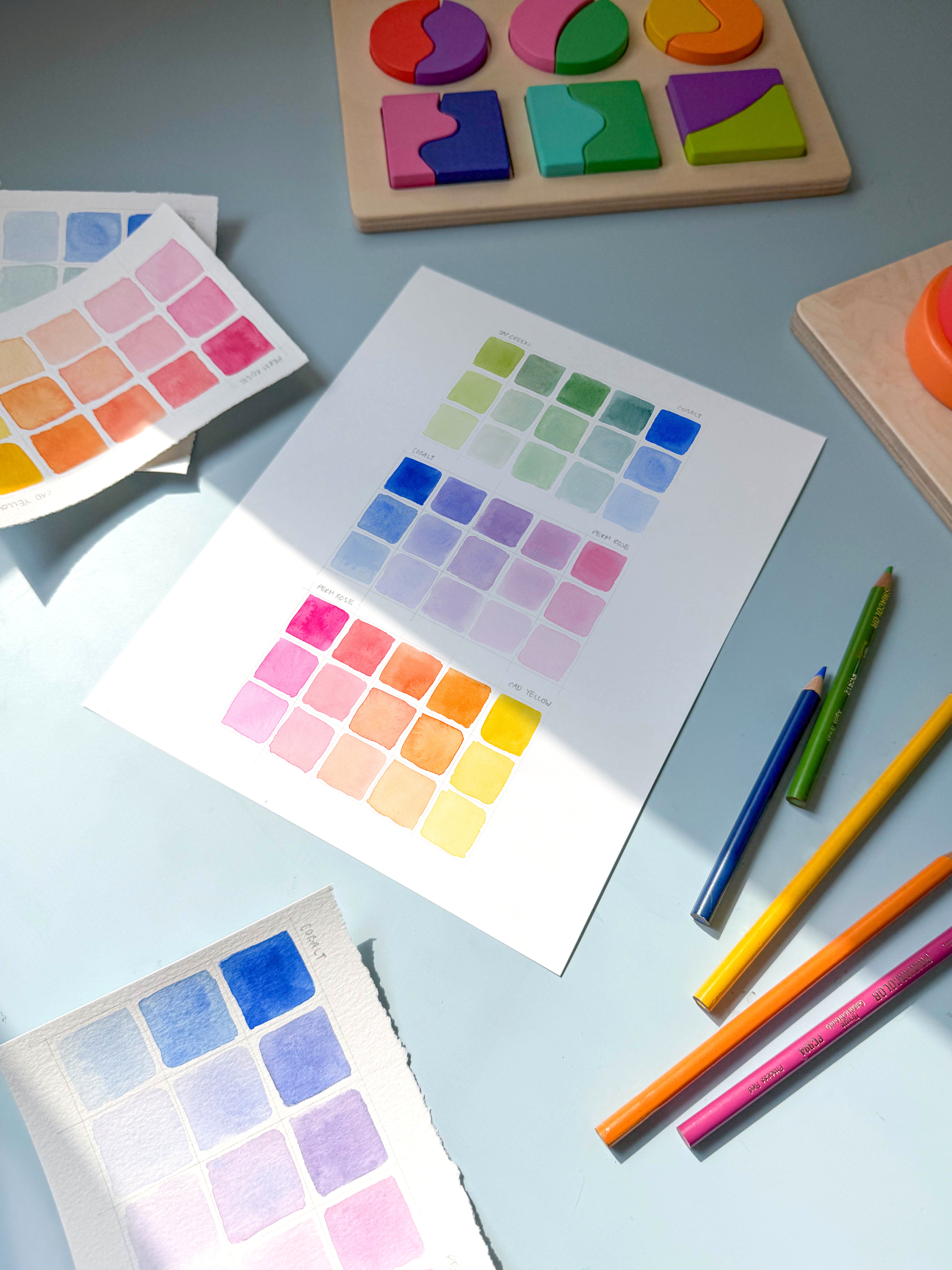 color swatch watercolor archival print by Katie Sinclair on a desk with colored pencils and a wooden puzzle.