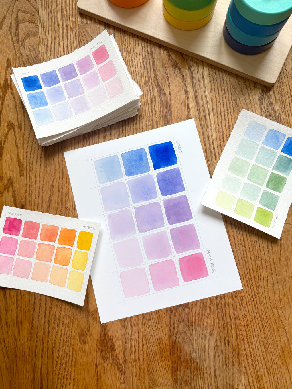pink and blue color swatch watercolor art print, surrounded by geometric toys on a wooden surface