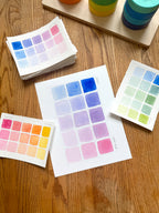 pink and blue color swatch watercolor art print, surrounded by geometric toys on a wooden surface