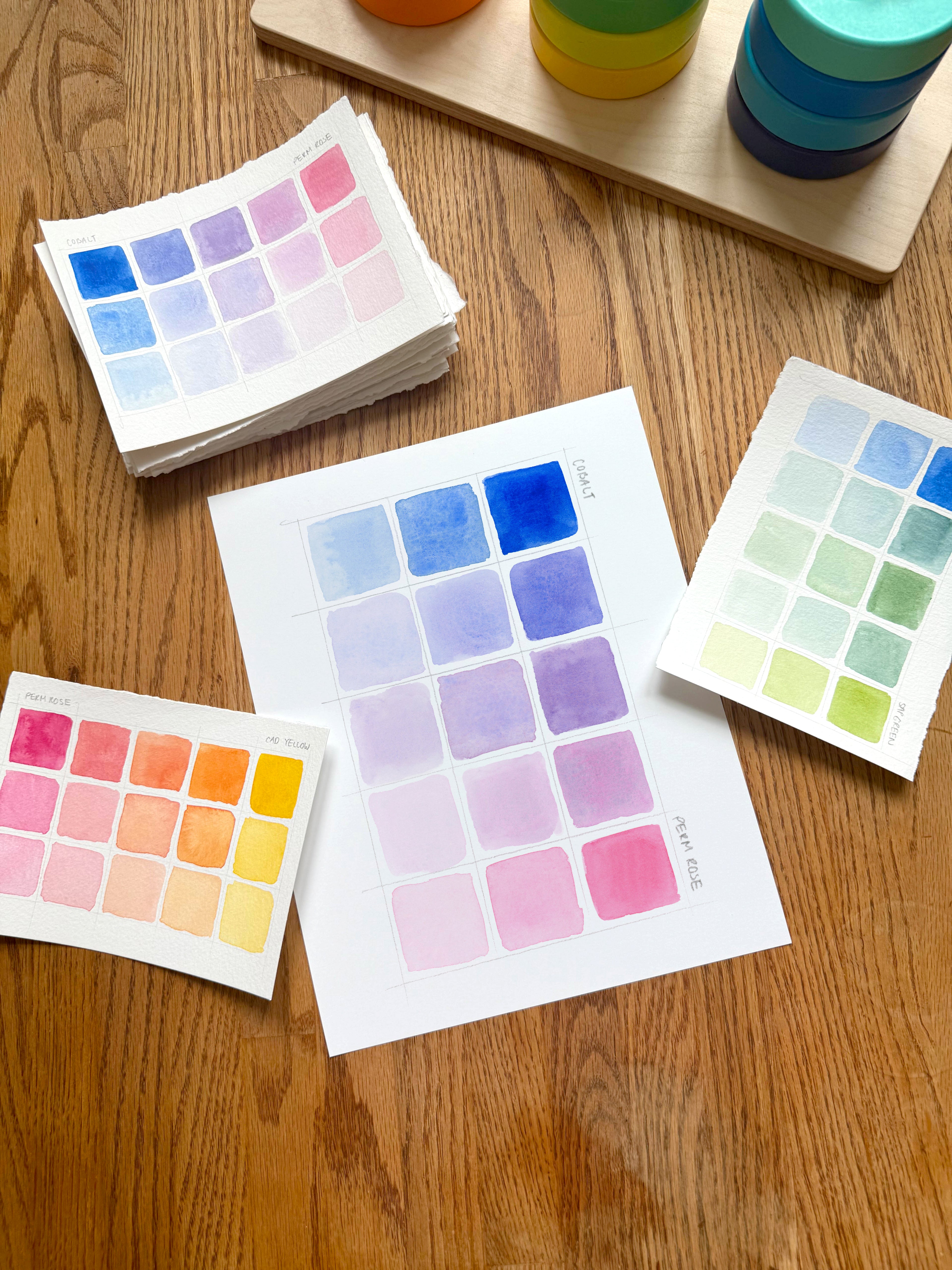 pink and blue color swatch watercolor art print, surrounded by geometric toys on a wooden surface