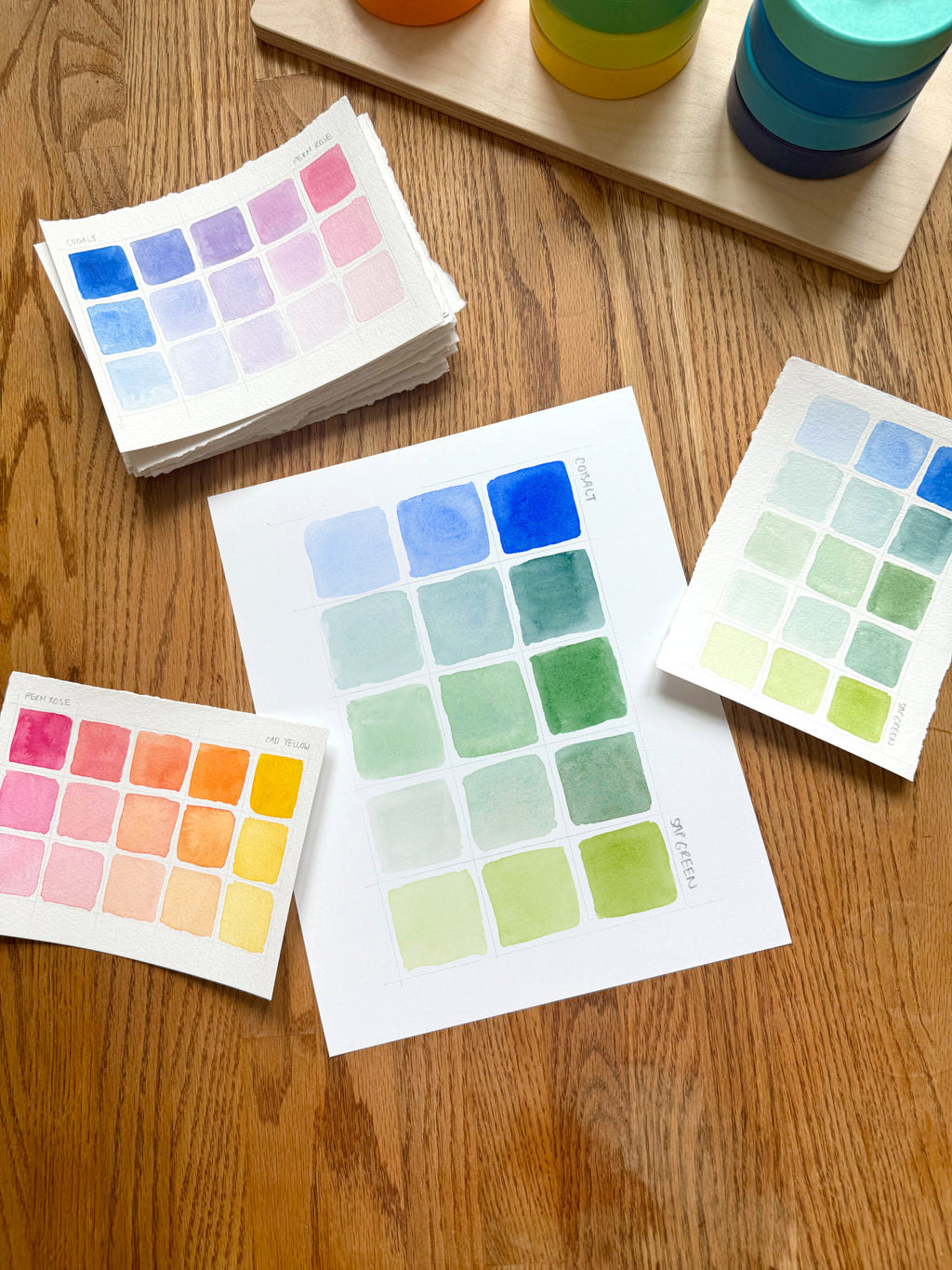 blue and green color swatch watercolor art print, surrounded by geometric toys on a wooden surface