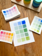 blue and green color swatch watercolor art print, surrounded by geometric toys on a wooden surface