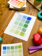 blue and green color swatch watercolor art print, surrounded by geometric toys on a wooden surface
