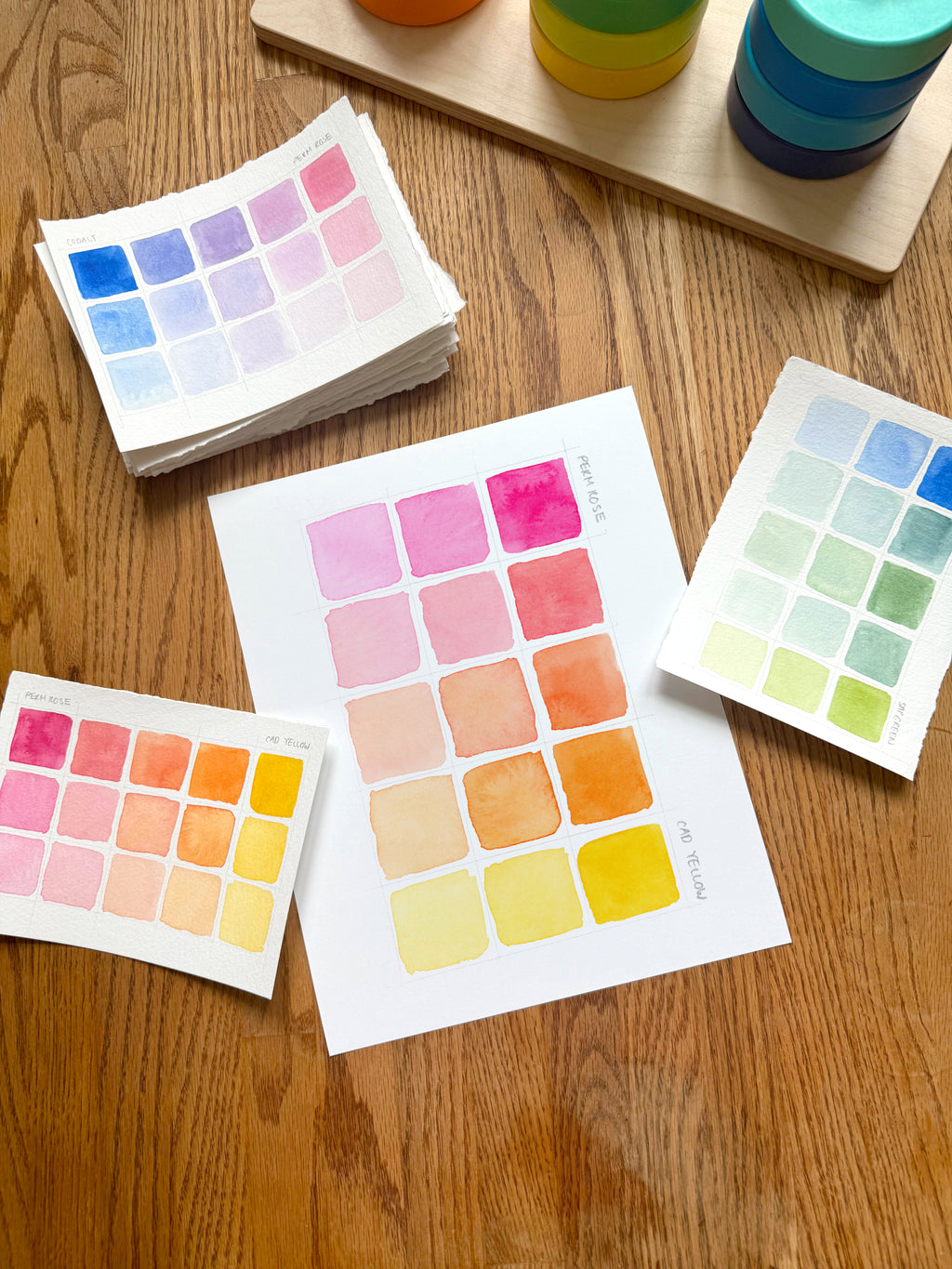 pink and yellow color swatch watercolor art print, surrounded by geometric toys on a wooden surface