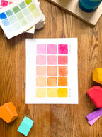 pink and yellow color swatch watercolor art print, surrounded by geometric toys on a wooden surface