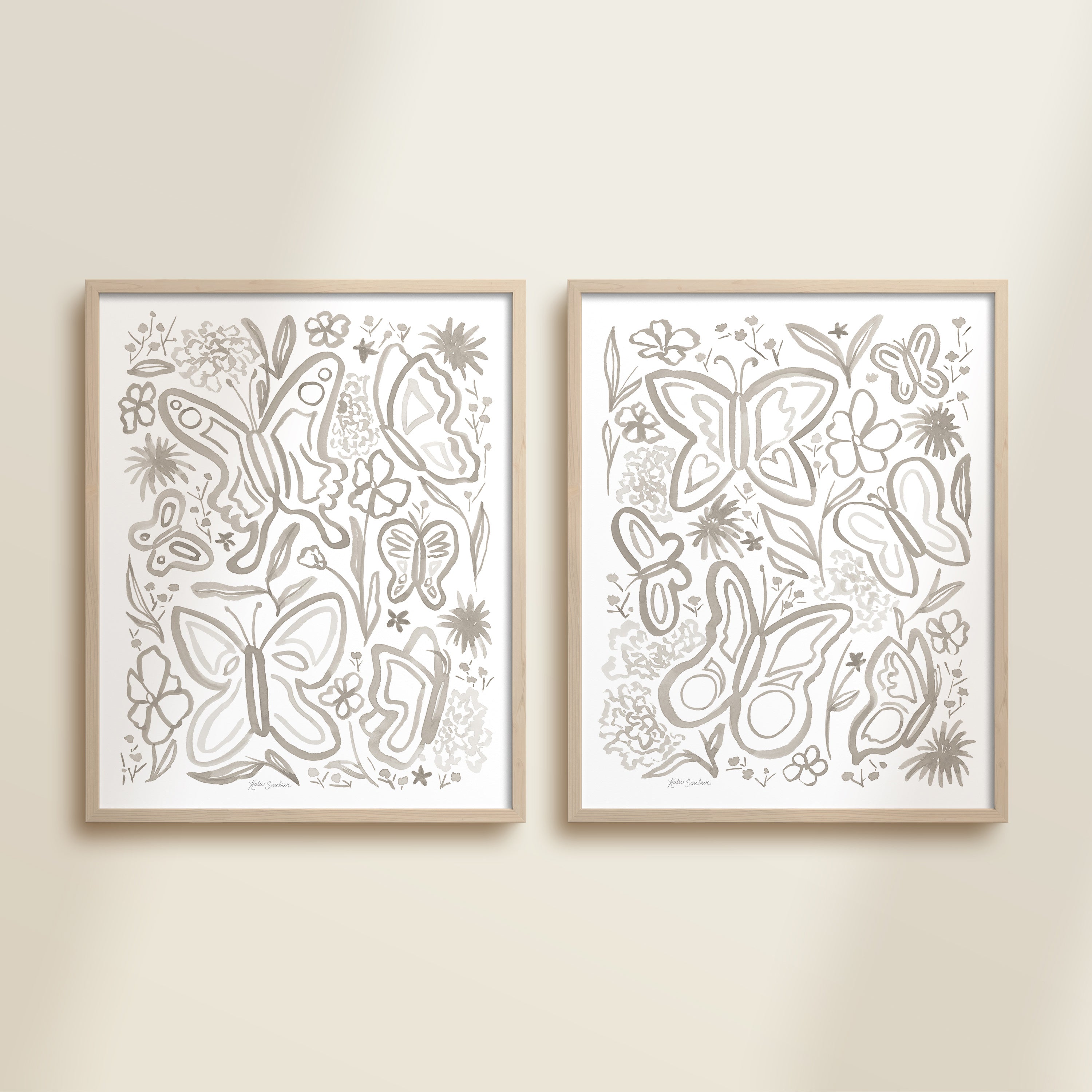 Two framed gray watercolor garden-themed artworks on a beige wall, featuring a butterflies and flowers.