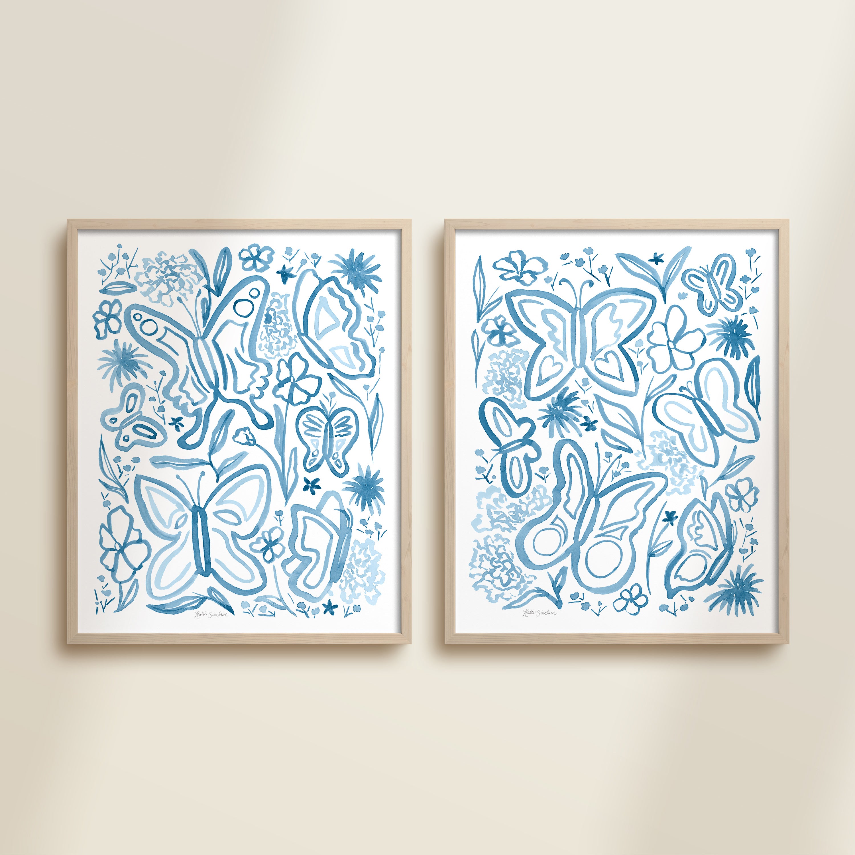 Two framed blue watercolor garden-themed artworks on a beige wall, featuring a butterflies and flowers.