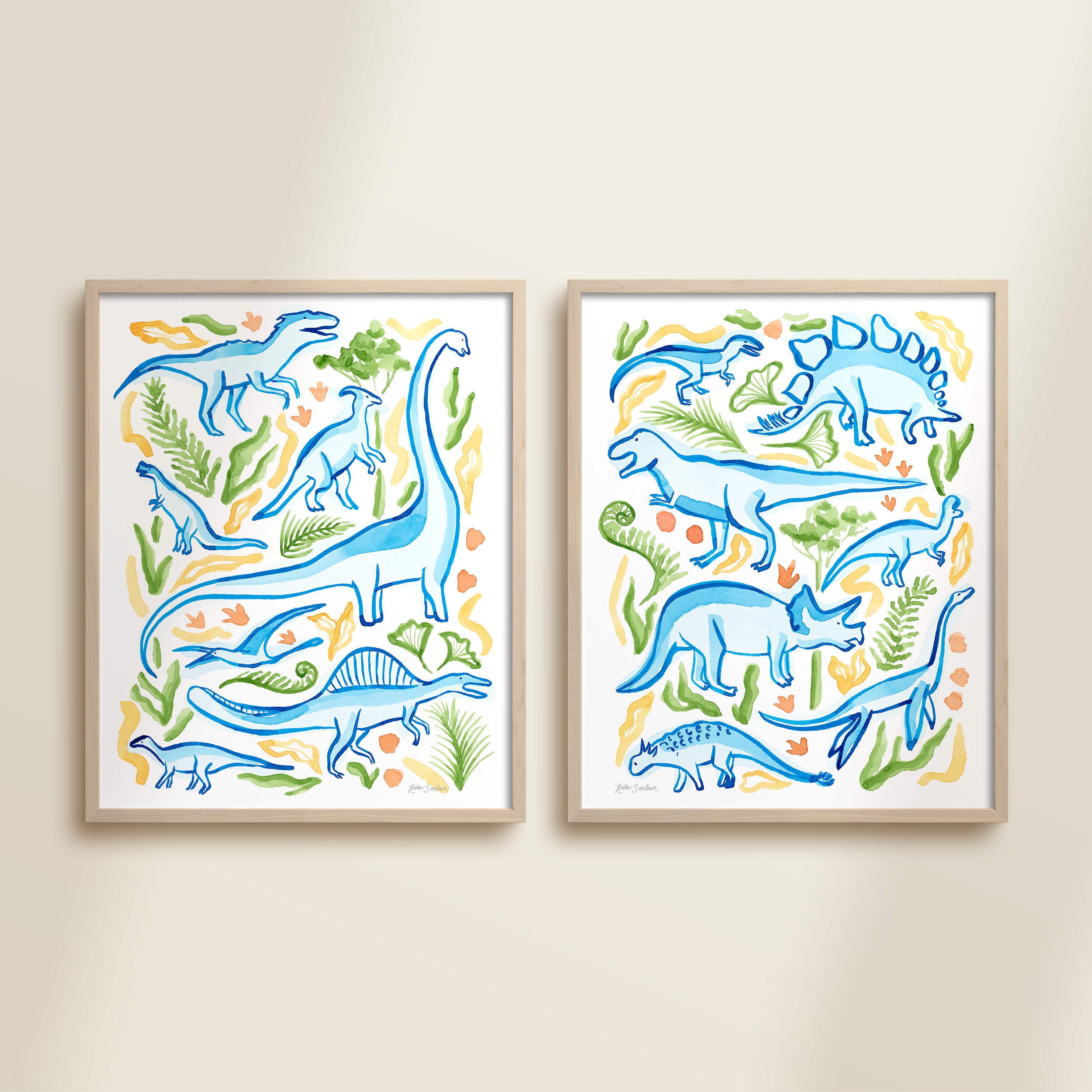 Two framed colorful blue, green, and yellow watercolor dinosaur-themed artworks on a beige wall, featuring a brontosaurus, t-rex, triceratops, raptor, spinosaurus, and plants.
