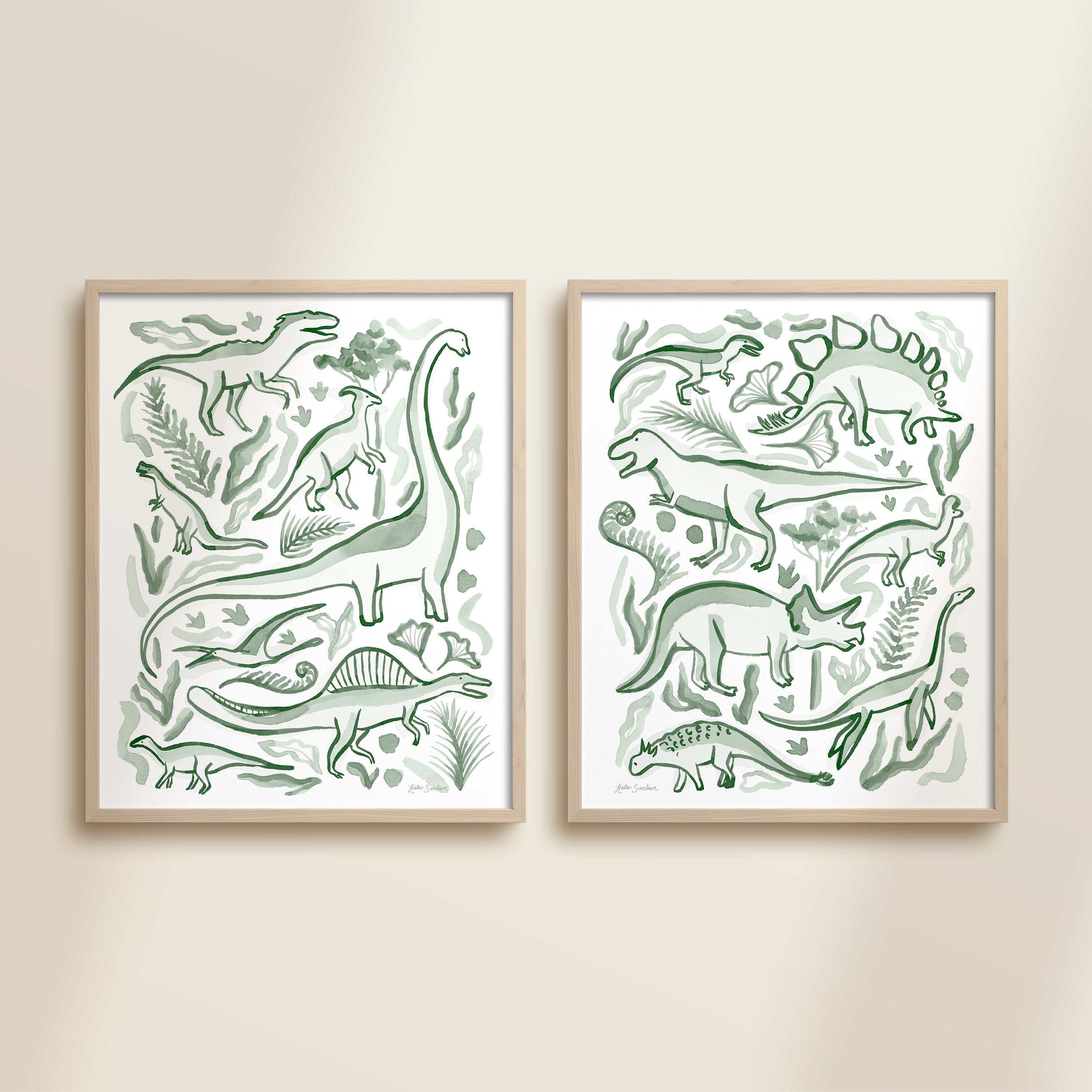 Two framed green watercolor dinosaur-themed artworks on a beige wall, featuring a brontosaurus, t-rex, triceratops, raptor, spinosaurus, and plants.