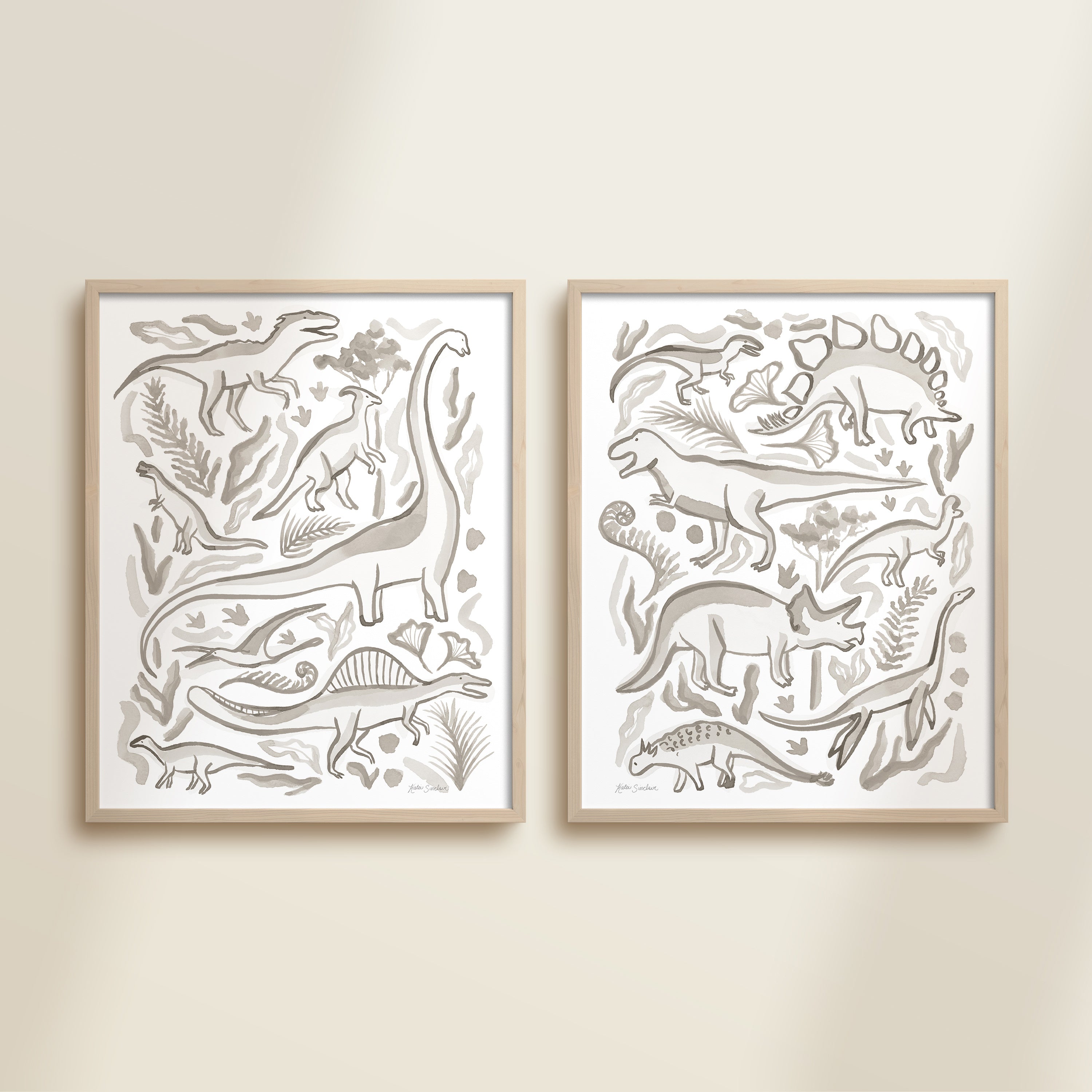 Two framed gray watercolor dinosaur-themed artworks on a beige wall, featuring a brontosaurus, t-rex, triceratops, raptor, spinosaurus, and plants.