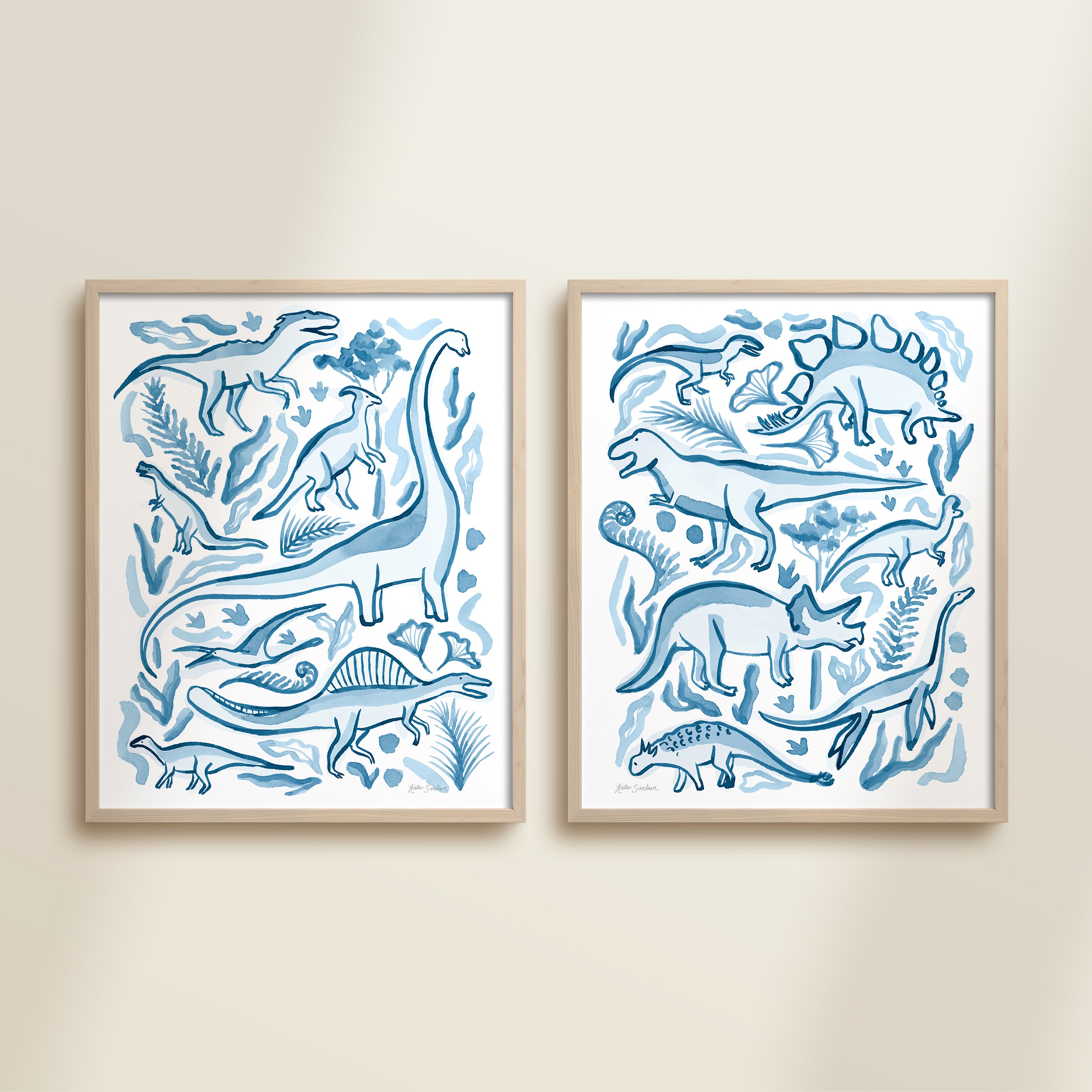Two framed blue watercolor dinosaur-themed artworks on a beige wall, featuring a brontosaurus, t-rex, triceratops, raptor, spinosaurus, and plants.