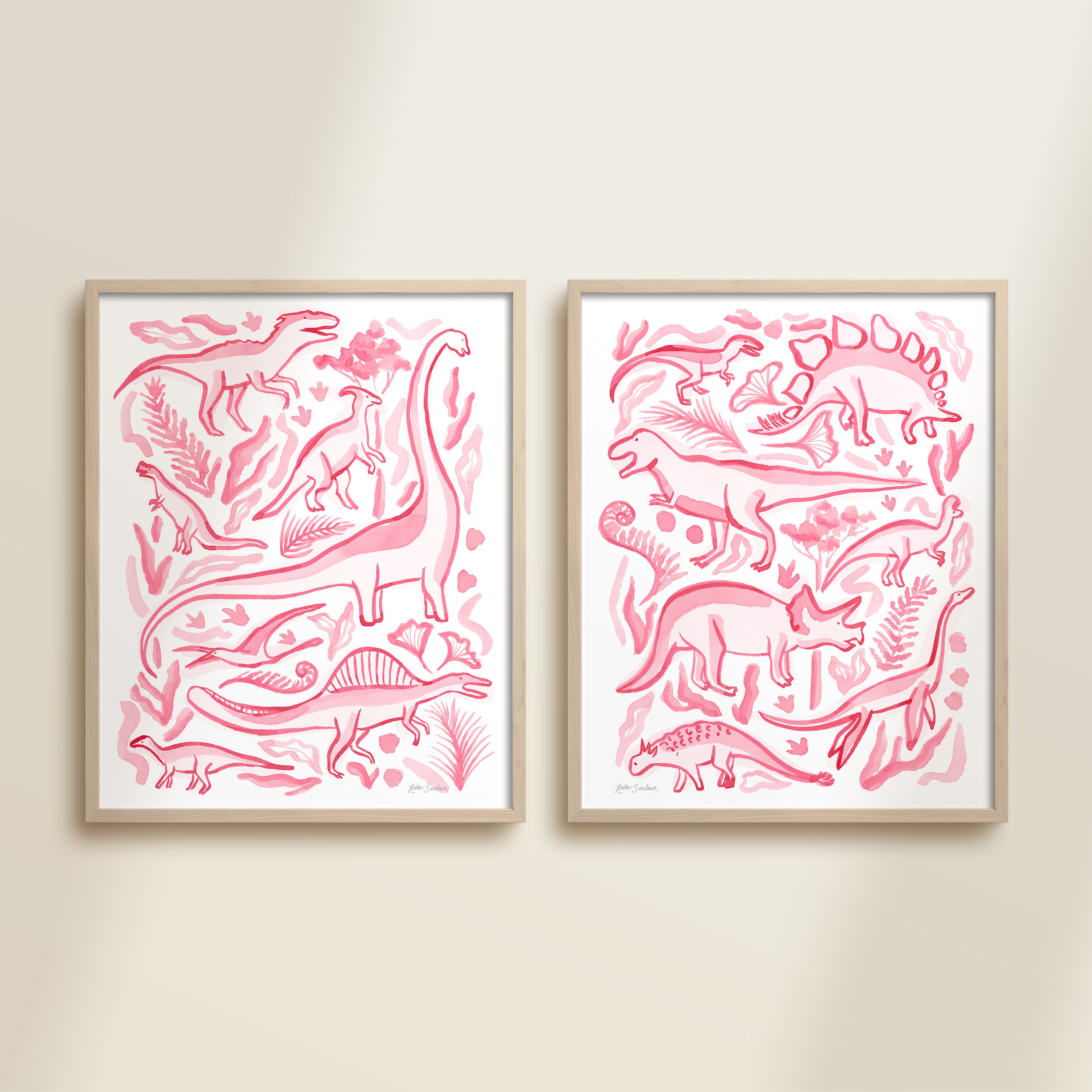 Two framed pink watercolor dinosaur-themed artworks on a beige wall, featuring a brontosaurus, t-rex, triceratops, raptor, spinosaurus, and plants.