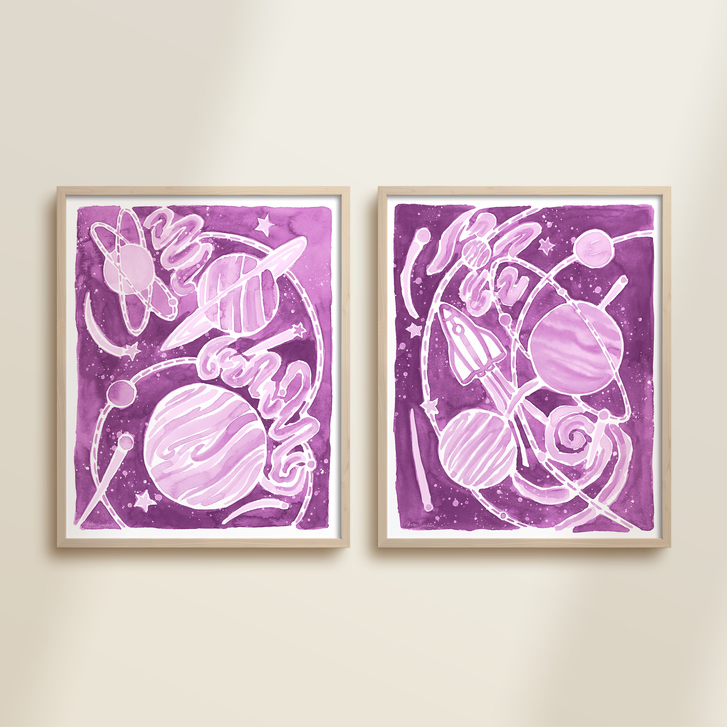 Two framed purple watercolor space-themed artworks on a beige wall, featuring planets, spaceships, stars, and a galaxy.