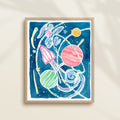 Framed colorful watercolor artwork of space-themed design with planets, stars, and a rocket ship.
