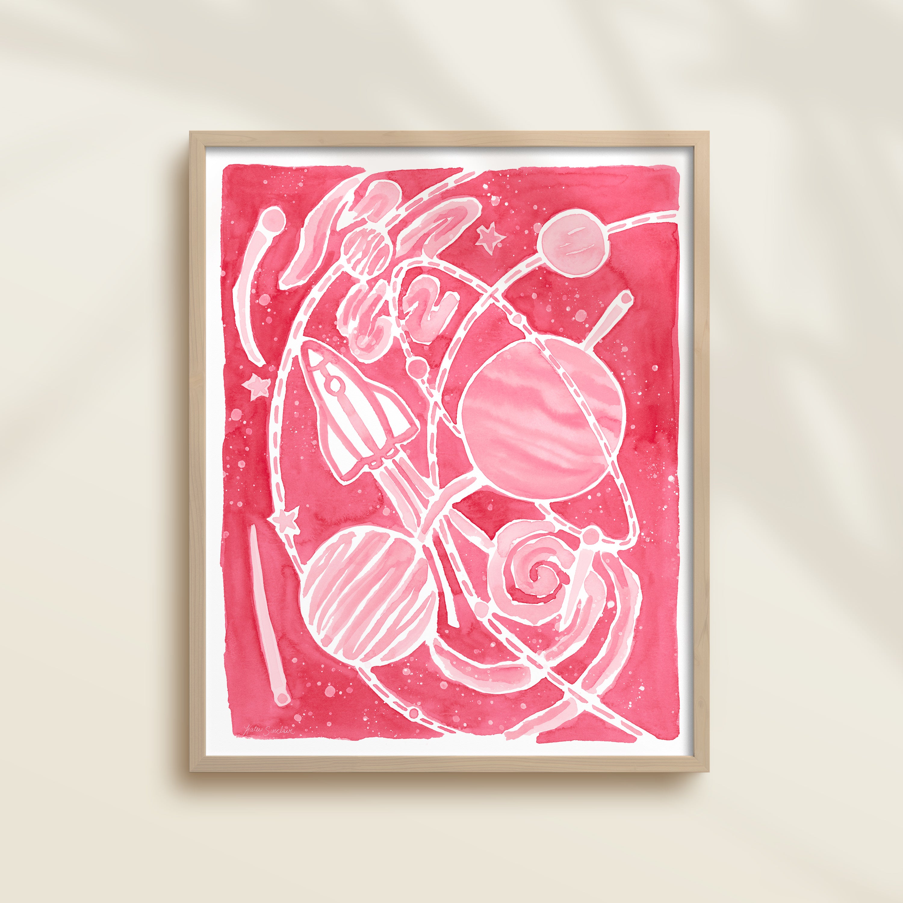 Framed pink watercolor artwork of space-themed design with planets, stars, and a rocket ship.