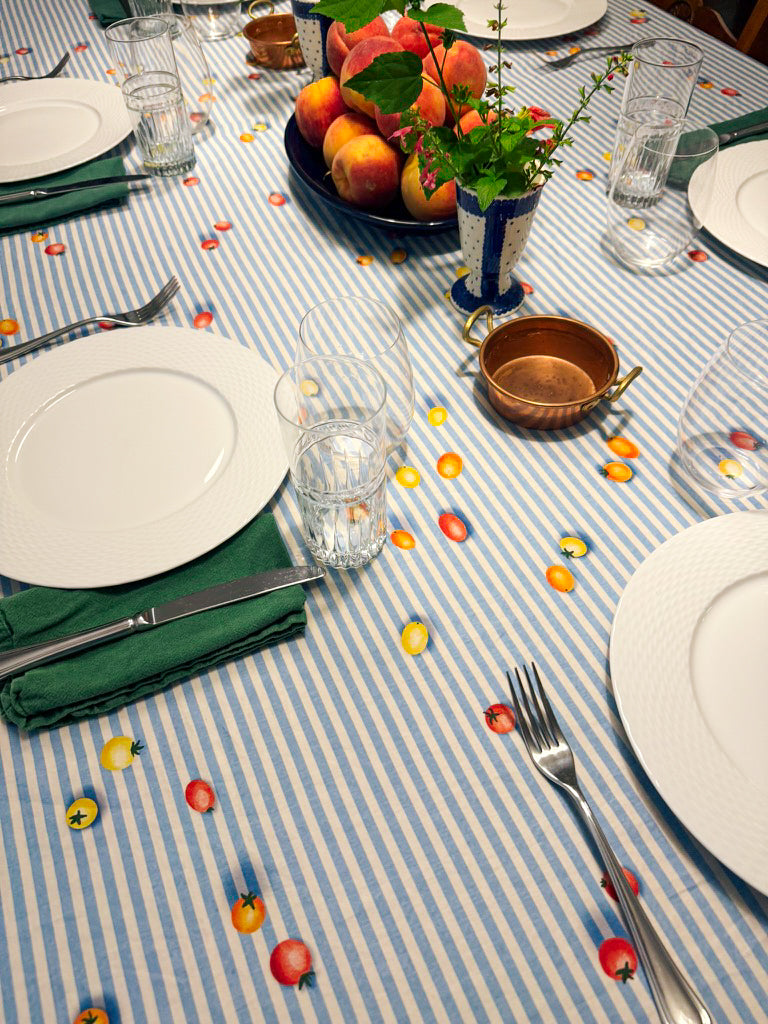 Dining table setting with plates, glasses, and decorative items on a striped tablecloth with tomatoes, designed by Katie Sinclair.