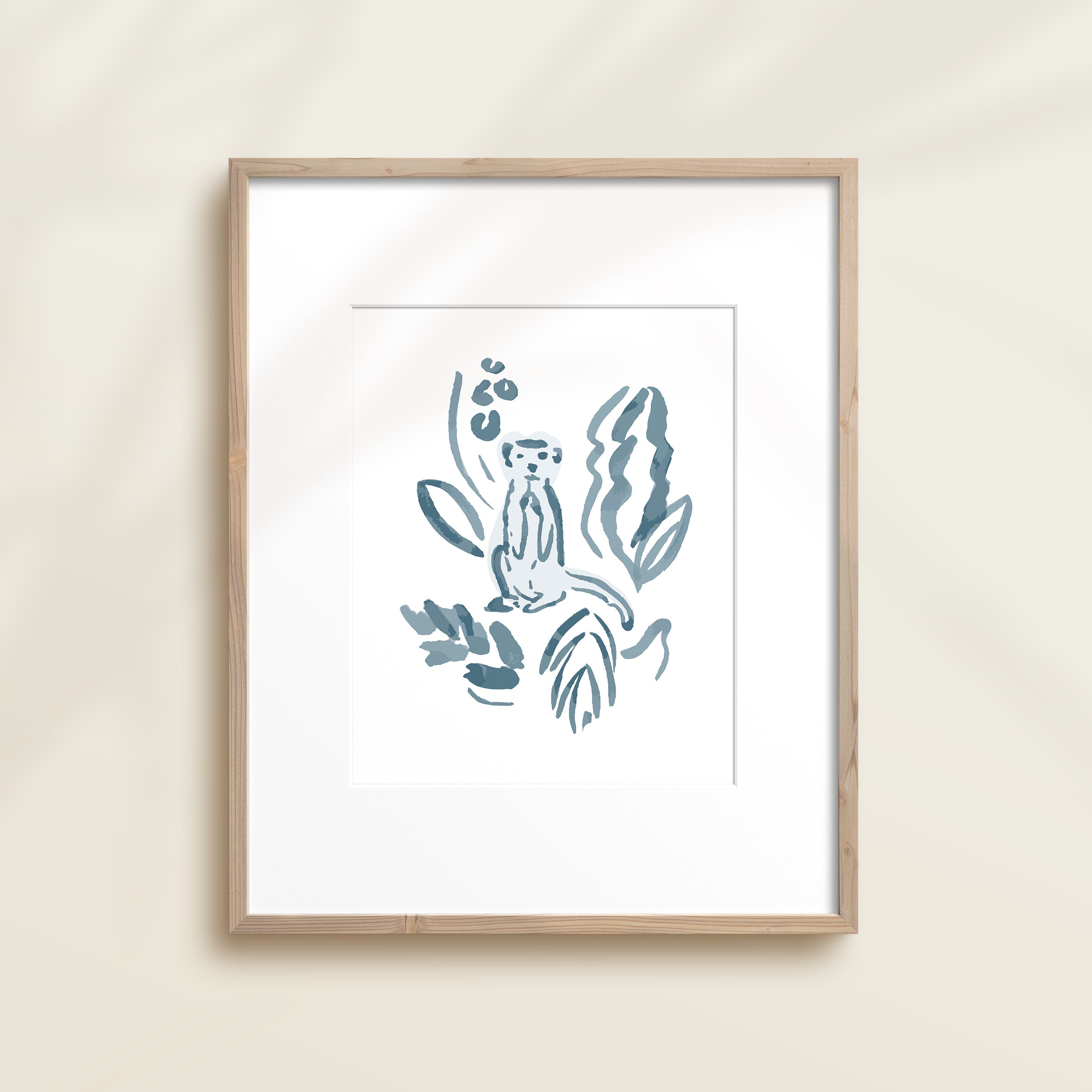 A framed watercolor print by Katie Sinclair of a meercat surrounded by  foliage, displayed on a wall.  This image showcases the blue color version.