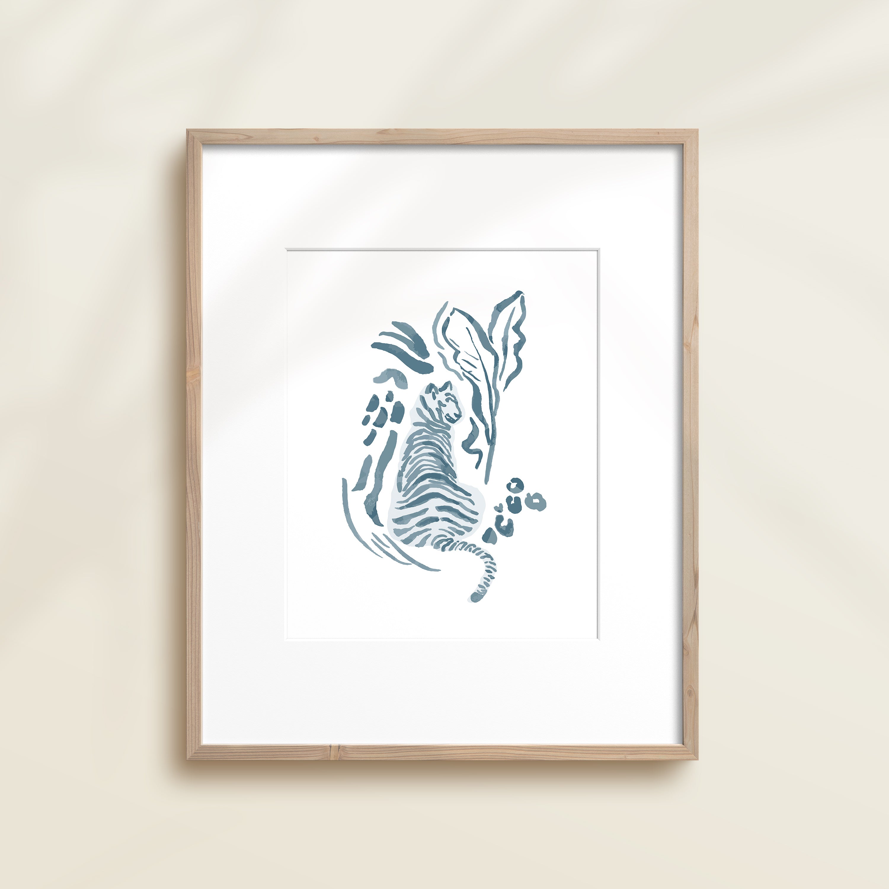 A framed watercolor print by Katie Sinclair of a tiger surrounded by  foliage, displayed on a wall.  This image showcases the blue color version.