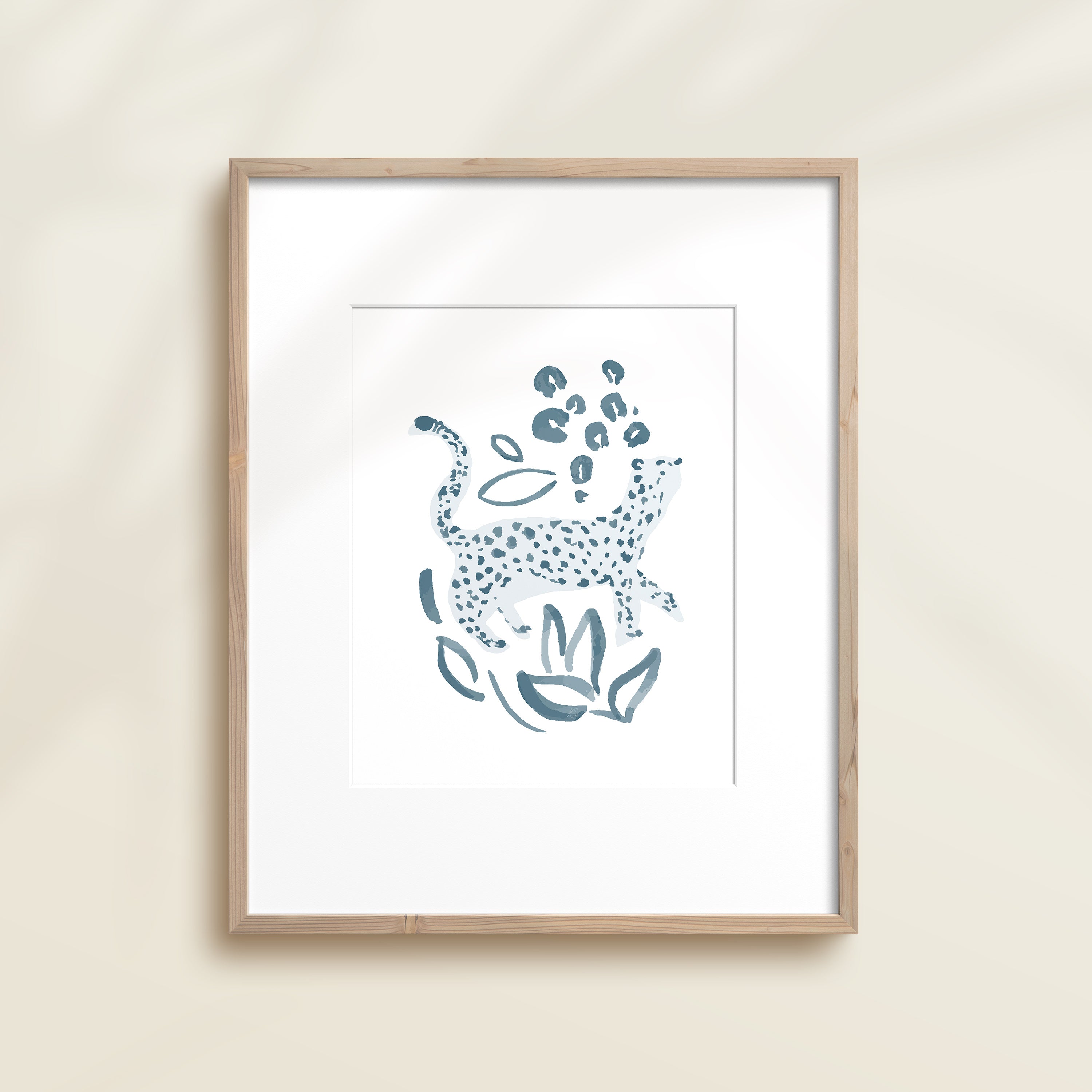 A framed watercolor print by Katie Sinclair of a cheetah surrounded by  foliage, displayed on a wall.  This image showcases the blue color version.