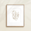 A framed watercolor print by Katie Sinclair of an crocodile surrounded by  foliage, displayed on a wall.  This image showcases the gray color version.