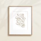 A framed watercolor print by Katie Sinclair of an bird surrounded by  foliage, displayed on a wall.  This image showcases the gray color version.