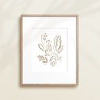 A framed watercolor print by Katie Sinclair of an meercat surrounded by  foliage, displayed on a wall.  This image showcases the gray color version.
