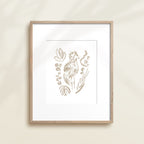 A framed watercolor print by Katie Sinclair of an tropical bird surrounded by  foliage, displayed on a wall.  This image showcases the gray color version.