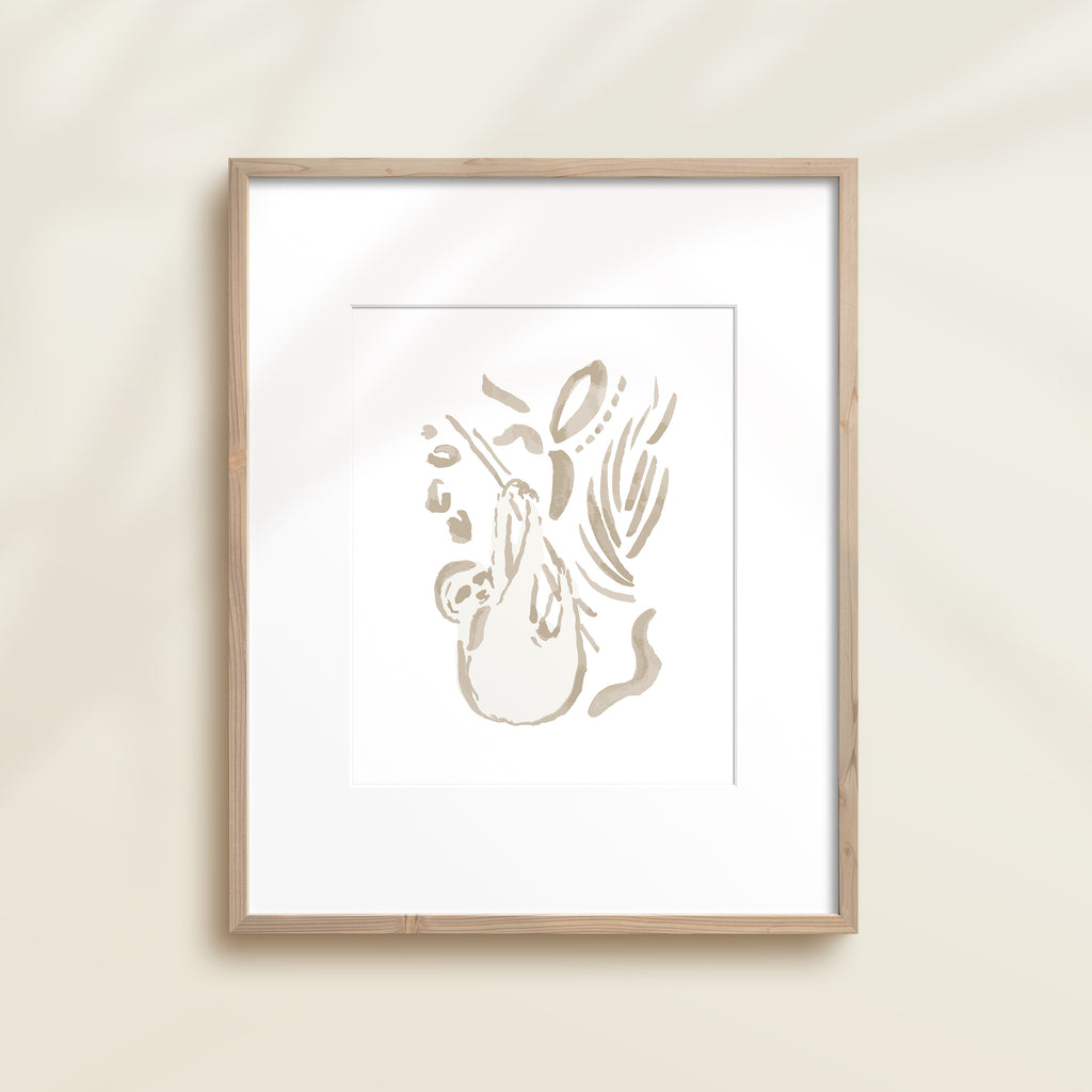 A framed watercolor print by Katie Sinclair of an sloth surrounded by  foliage, displayed on a wall.  This image showcases the gray color version.