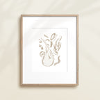 A framed watercolor print by Katie Sinclair of an sloth surrounded by  foliage, displayed on a wall.  This image showcases the gray color version.