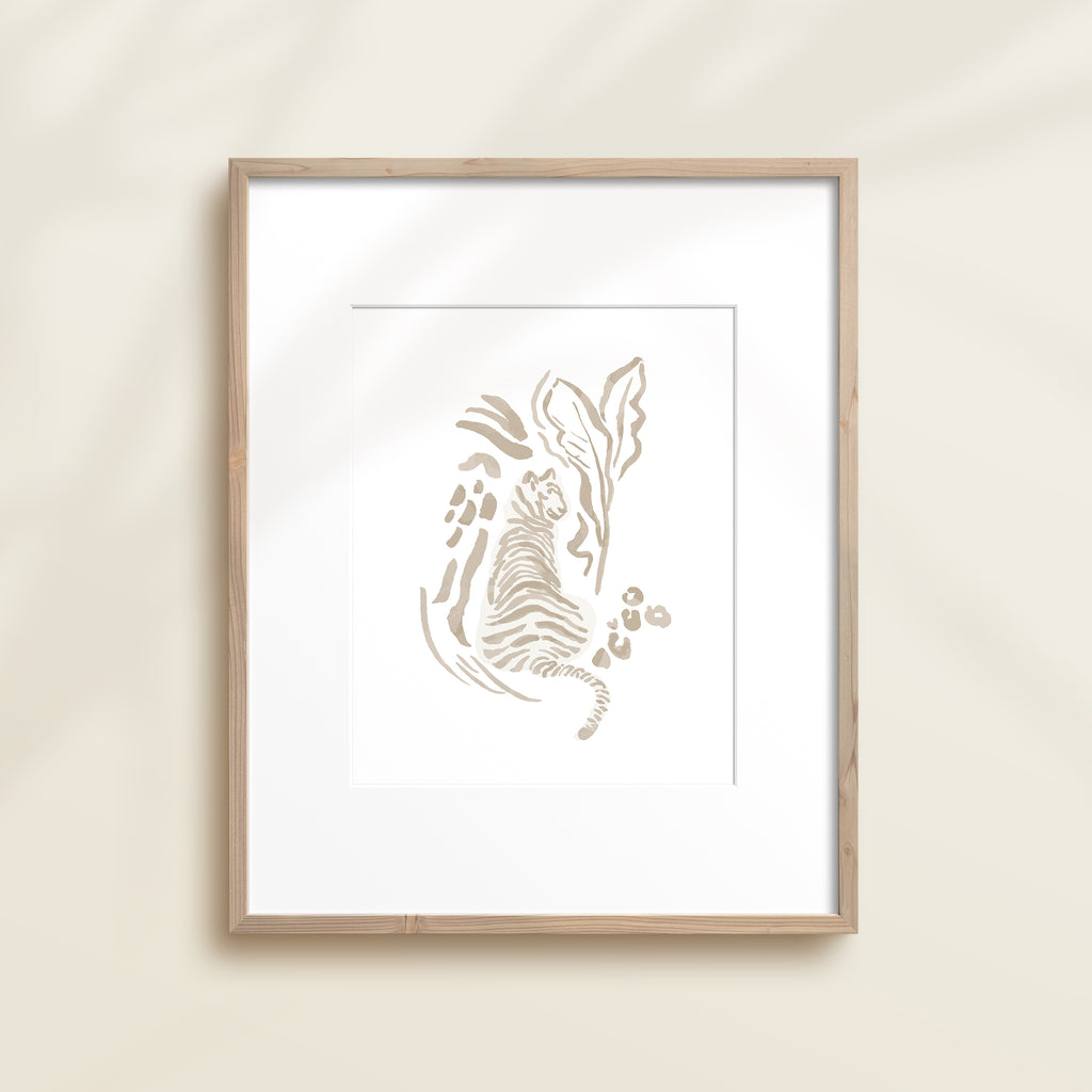 A framed watercolor print by Katie Sinclair of an tiger surrounded by  foliage, displayed on a wall.  This image showcases the gray color version.