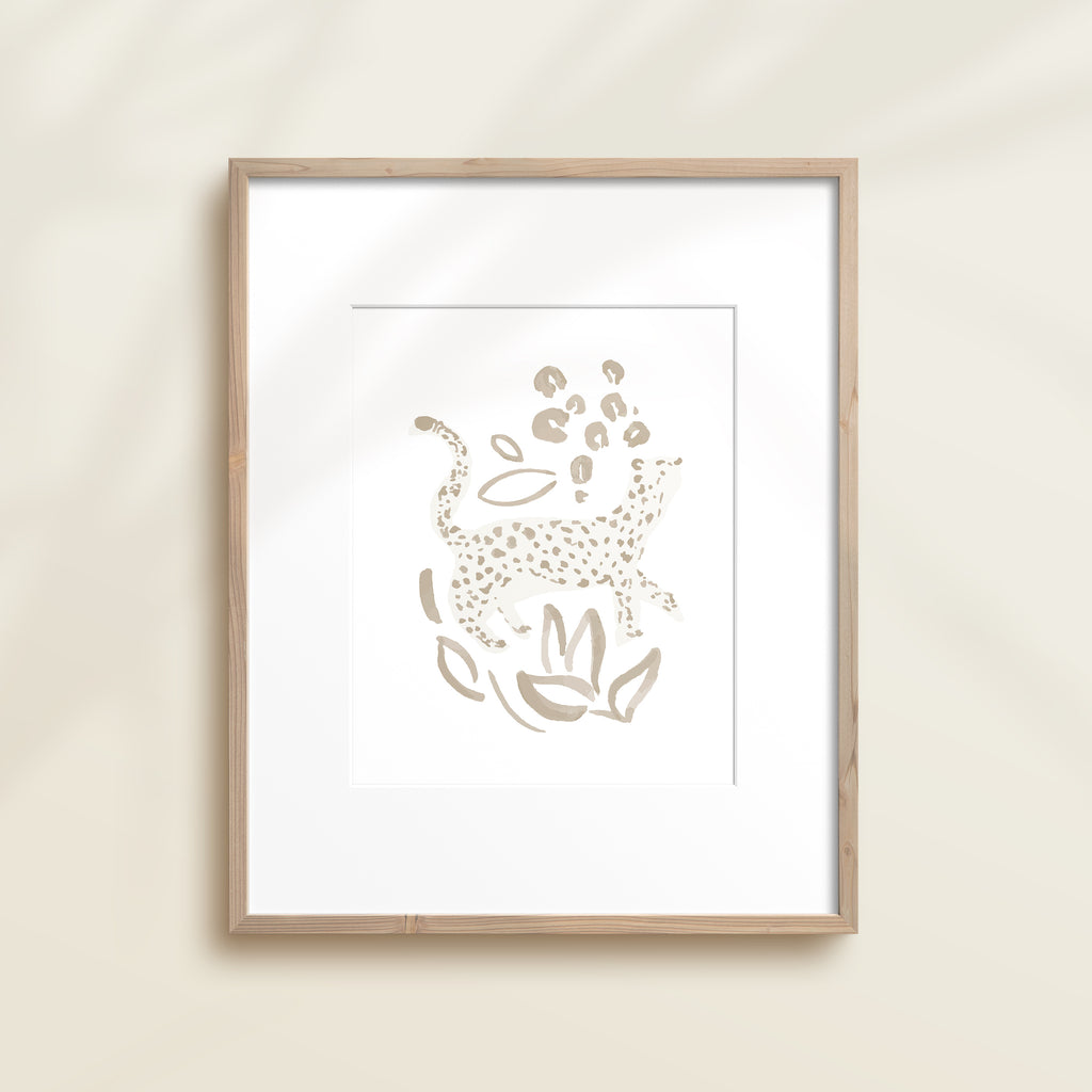 A framed watercolor print by Katie Sinclair of an cheetah surrounded by  foliage, displayed on a wall.  This image showcases the gray color version.