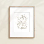 A framed watercolor print by Katie Sinclair of an cheetah surrounded by  foliage, displayed on a wall.  This image showcases the gray color version.