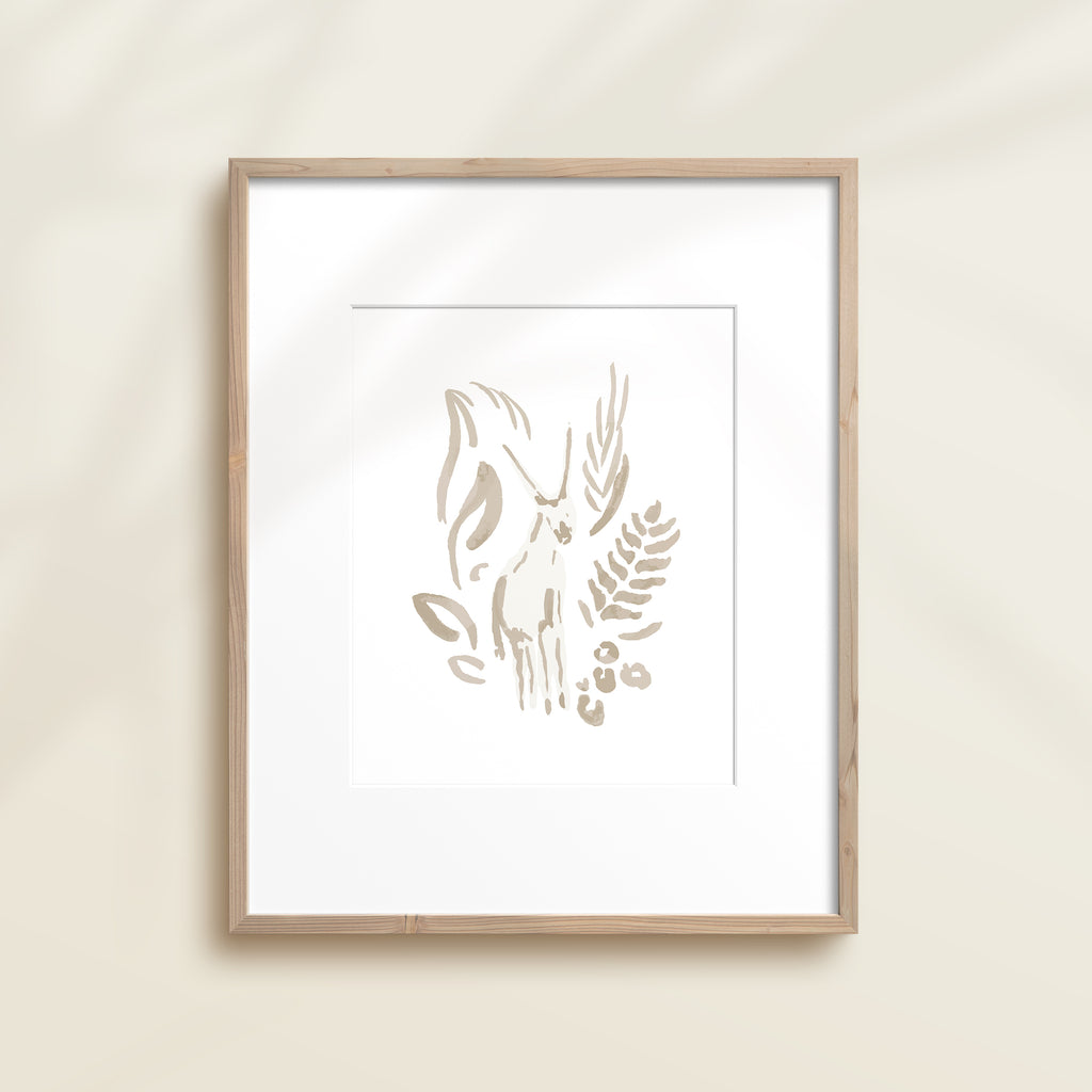 A framed watercolor print by Katie Sinclair of an antelope surrounded by  foliage, displayed on a wall.  This image showcases the gray color version.