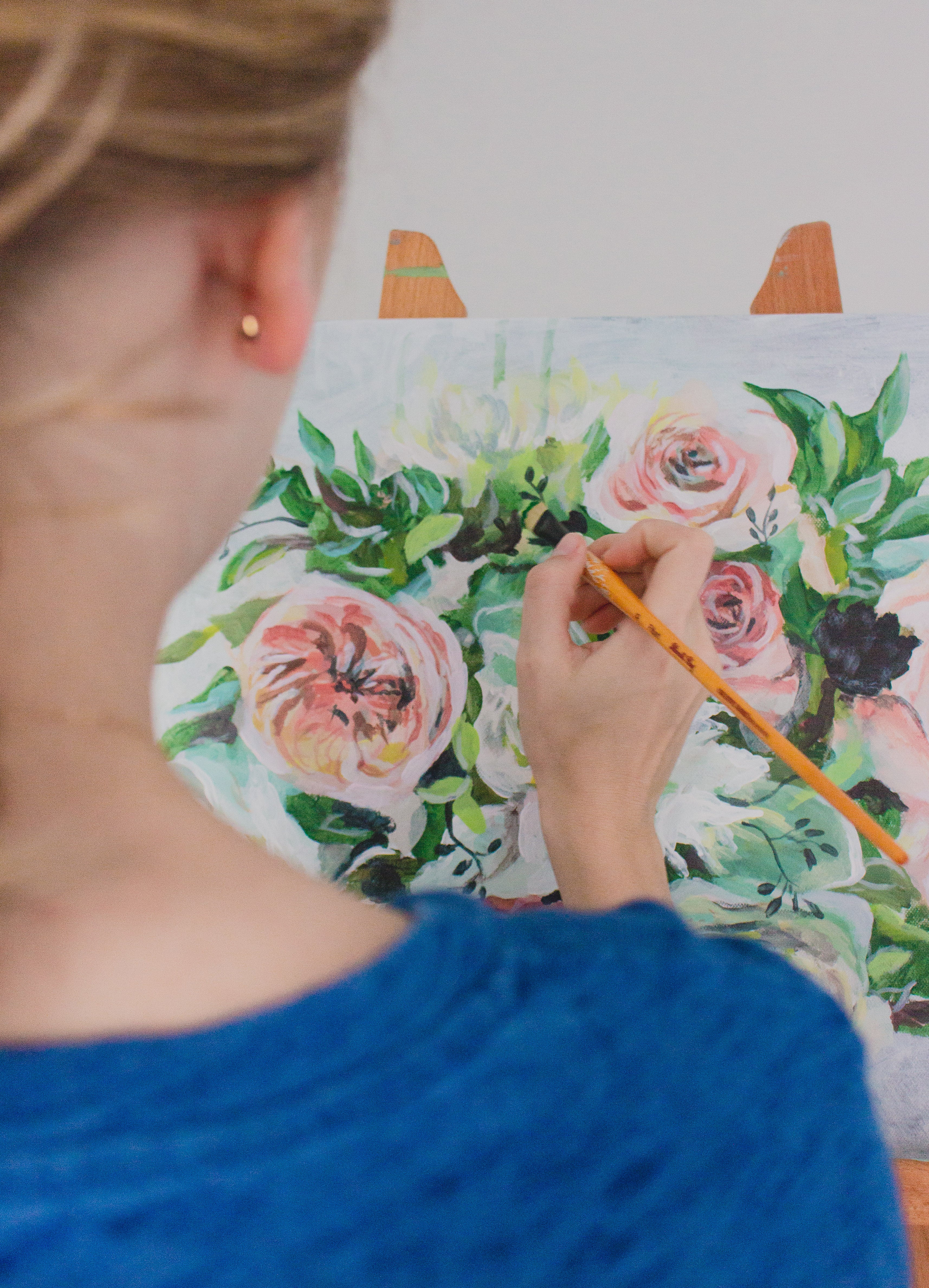 Person painting a floral design on a canvas with a paintbrush.